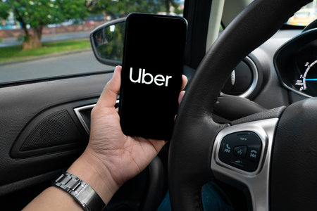 Uber driver holding smartphone in car. Uber is an American company offering transportation services...