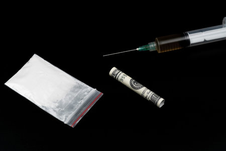 Cocaine or other illegal drugs, white powder, syringe, isolated on black glossy background