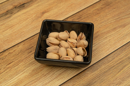 Pistachios on a black plate with wooden background