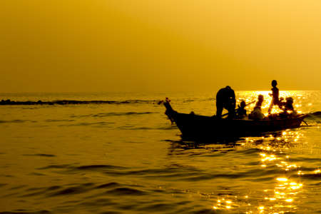 Silhouette fisherman family on the boat in sunset, returning to home after fishing の写真素材