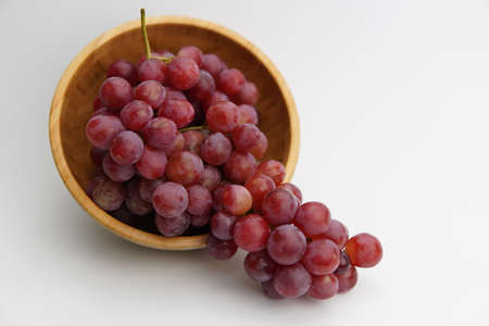 Fresh and ripe red grapes in a wooden bowl, isolated in white background. Bunch of raw and juicy grapevines ..の写真素材