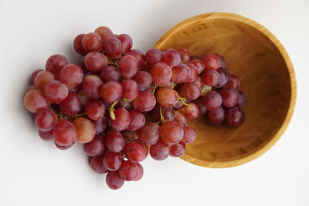 Fresh and ripe red grapes in a wooden bowl, isolated in white background. Bunch of raw and juicy grapevines ..の写真素材