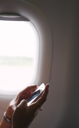 woman hand holding smartphone and texting during flight on air plane near windowの写真素材