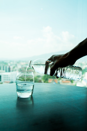 hand pouring water from bottle to glass with city backgroundの写真素材