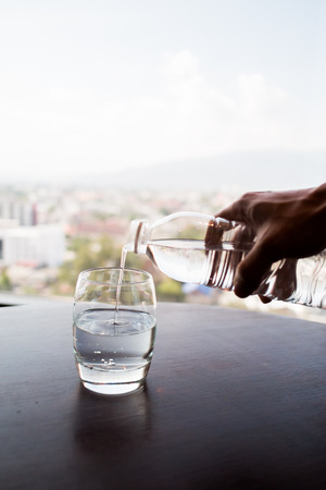 hand pouring water from bottle to glass with city backgroundの写真素材