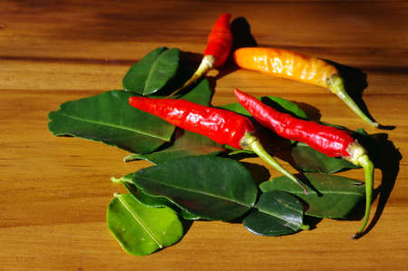 Fresh raw red chilies and kaffir lime leaves on the wood table.の写真素材