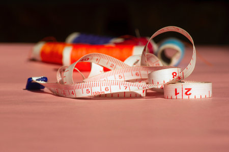 Colorful sewing threadsand a tape measure on pink background