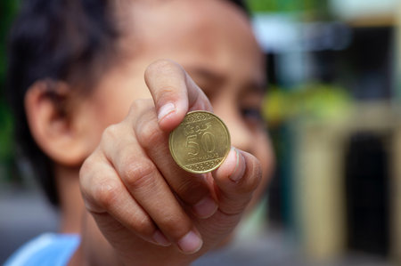 Asian child's hand holding a Fifty Halalas Riyal coin, Saudi Arabia money, selected focusの写真素材