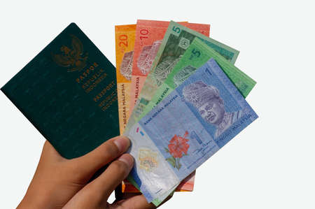 Hands holding Ringgit Malaysia money and an Indonesian passport book, shallow focus and isolated on white background. The concept of immigrant employees from Indonesiaの写真素材