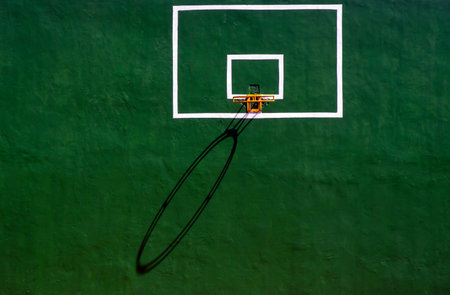 Basketball ring with its shadow on the green cement wall