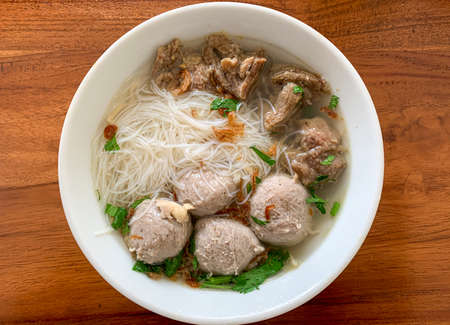 A bowl of meat ball soup with fresh vegetables on wooden tableの写真素材