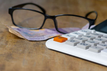 Glasses, money and a calculator lying on wooden vintage tableの写真素材