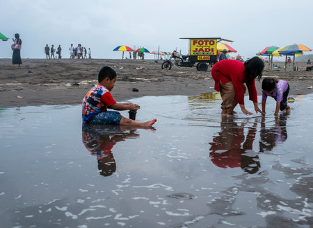 Yogyakarta, Indonesia - May 6, 2023: Indonesian children playing in the sand on Parangtritis Beach, Yogyakarta, Indonesiaのeditorial素材