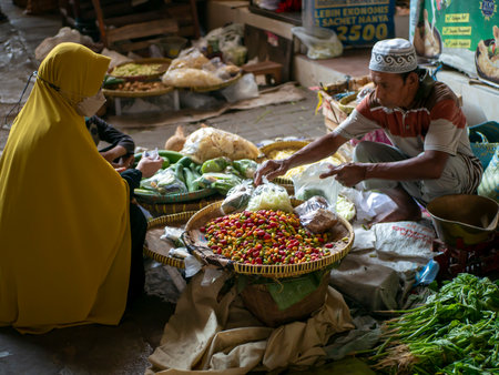 Yogyakarta-Indonesia, June 17, 2023: An old man selling vegetables to a female buyer at a traditional market in Bantul, Yogyakarta, Indonesiaのeditorial素材