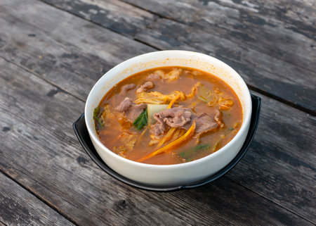Beef Tomyam, spicy, salty, sour soup, Asian traditional food, in a white bowl on an old wooden tableの写真素材