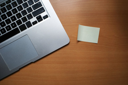 A business desk table with a laptop and a sticky note paper. Wood background with copy space.