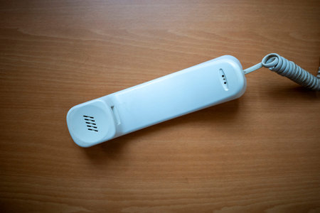 White handset of landline phone on wooden table. Telecomunication concept background.