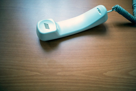 White handset of landline phone on wooden table. Telecomunication concept background.