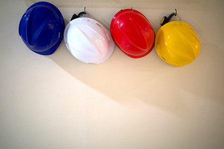 Four colorful safety helmets representing blue, white, red and yellow color on a concrete wall....
