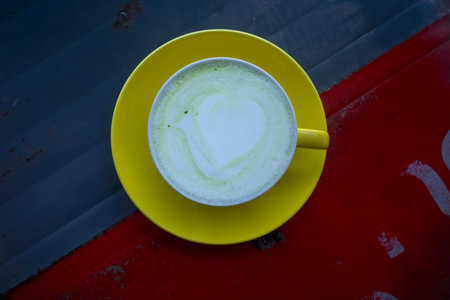 Matcha green tea latte with latte art served in a yellow handmade ceramic cup.