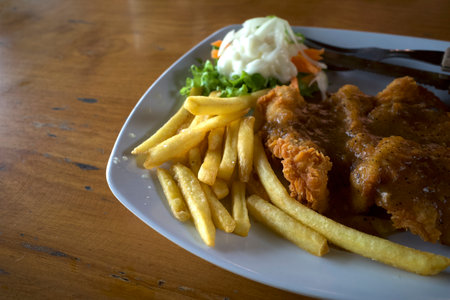 Fried chicken, French fries and vegetables on a white plate, on old wooden table, Indonesian cuisine, Indonesian food.の写真素材