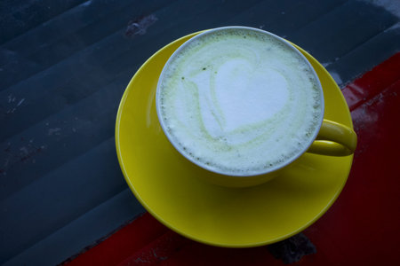 Matcha green tea latte with latte art served in a yellow handmade ceramic cup on a vintage metal...