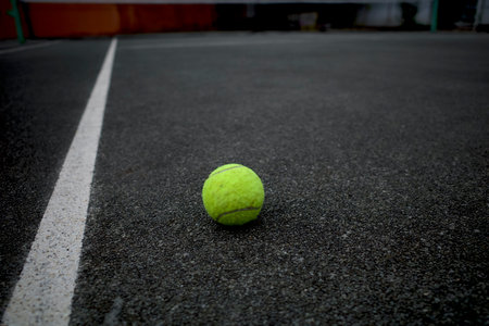 A bright green tennis ball near on white line of dark grey tennis court.の写真素材