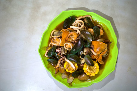 A variety of clams, crab, shrimp, squid and vegetables dishes with sauce on a green plate.