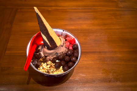 Ice cream in a classic bowl with a cone garnish, chocolate balls, nuts, pudding and watermelon, on a wooden table.の写真素材