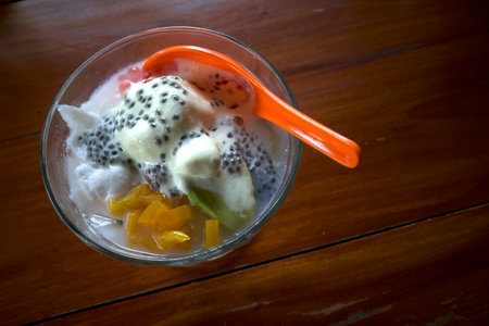 A bowl of creamy ice cream and an orange spoon, garnished with basil seeds and sweet jackfruits.の写真素材