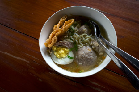 A bowl of meatball soup with fresh vegetables and an egg on the old wooden table.の写真素材