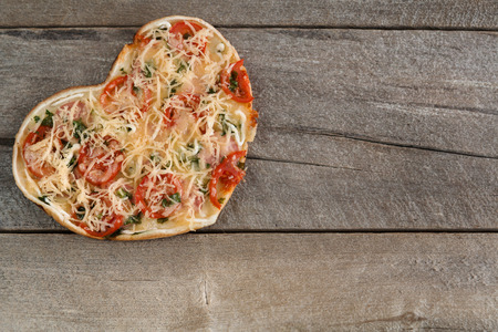 Pizza for Valentine's day with cheese, garlic parsley and pepper on old wooden backgroundの写真素材