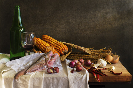 Still life Photography with cook, fish,corn,cob,  red wine on wooden table and breadの写真素材
