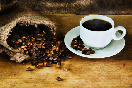 Hot Coffee cup and roast coffee beans on a wooden table. Dark background.の写真素材
