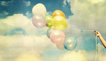 Girl hand holding multi colored balloons done with a retro vintage, concept of happy birth day in summer and wedding honeymoon party (Vintage color tone)の写真素材