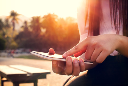 Close up of a woman using mobile smart phone in sunset with outdoor, nature background. (vintage color tone)の写真素材