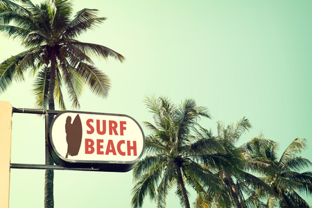 Vintage surf beach signage and coconut palm tree on tropical beach blue sky with sunlight of morning in summer,  instagram filterの写真素材