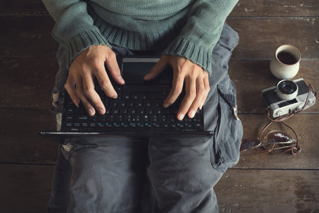 Top view male hands using Laptop with coffee cup, camera, eyeglass,  sitting on a wooden floor