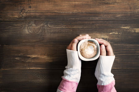 Above view of female hand holding hot cup of coffee on wood tableの写真素材