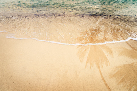 Palm tree shadow on the sandy beach with ocean wave - free space. vintage color tone effectの写真素材