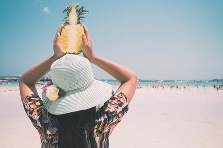 Fashion portrait rear of beautiful woman with fresh pineapple holds up - vacation on tropical beach...