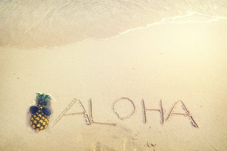 Inscription Aloha written on the sandy beach with ocean wave - free space. vintage color tone effect