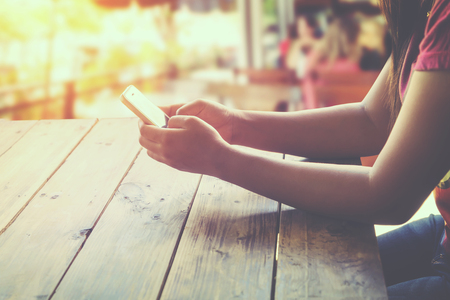 Side view of a woman using mobile smart phone in cafe sitting at wooden table outdoor area. coffee shop background. (vintage color tone)の写真素材