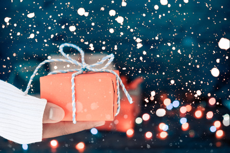 Woman hands holding Christmas handmade gift box with snow and bokeh light background. vintage color toneの写真素材