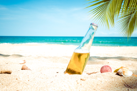 Beer bottle on a sandy beach with palm tree. vintage color tone effectの写真素材