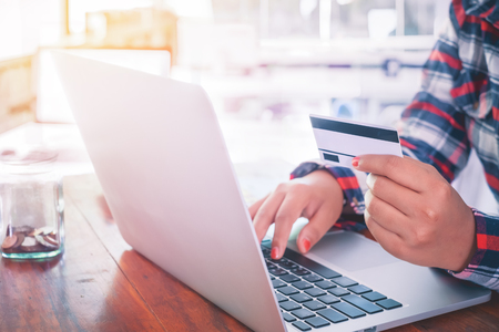 Hipster lifestyle - Side view shot of young business woman working on her laptop and using credit card sitting at wooden table in modern business office with vintage filter color toneの写真素材
