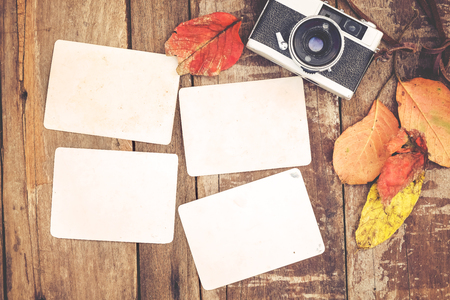 Retro camera and empty old instant paper photo album on wood table with maple leaves in autumn border design - concept of remembrance and nostalgia in fall season. vintage rustic style.の写真素材