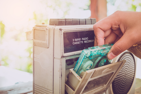 Retro lifestyle - Woman hand holding tape cassette with cassette player and recorder for listen music - vintage color tone effect.の写真素材