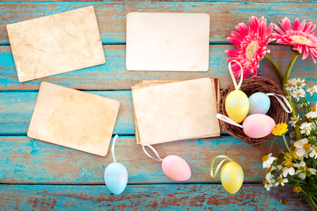 Colorful Easter eggs in nest with flower and empty old paper photo album on wood tableの写真素材