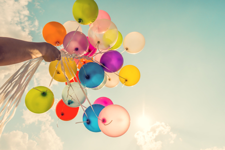 Hand holding multi colored balloons done with a retro vintage filter effect.の写真素材